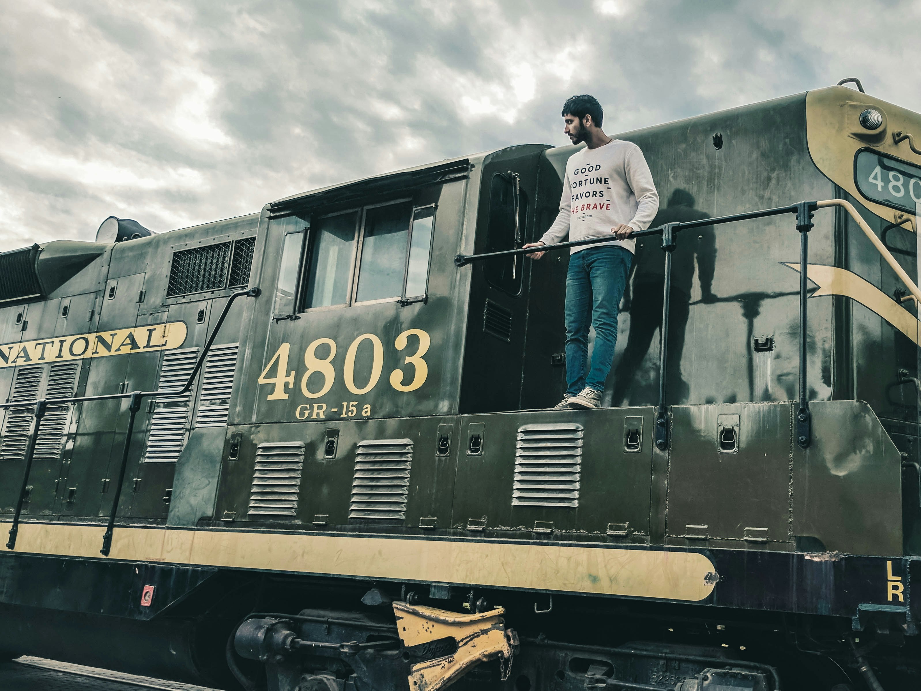 man in white long sleeve shirt and blue denim jeans standing on train during daytime